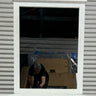 Person working with boxes and plastic sheeting inside a building reflected in a window.