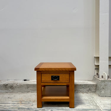 Wooden side table with a drawer against a plain wall.