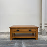 Wooden coffee table with two drawers on a gray floor against a white wall.