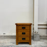 Wooden nightstand with three drawers against a plain wall.