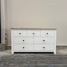 White dresser with black knobs on a gray floor against a plain wall