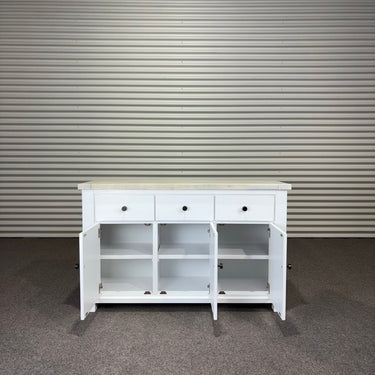 White wooden sideboard with open doors against a corrugated metal wall.