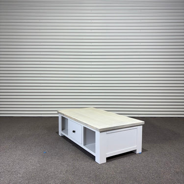 White coffee table with a light wood top against a corrugated metal wall.