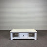 White wooden coffee table with a drawer against a gray corrugated metal wall.