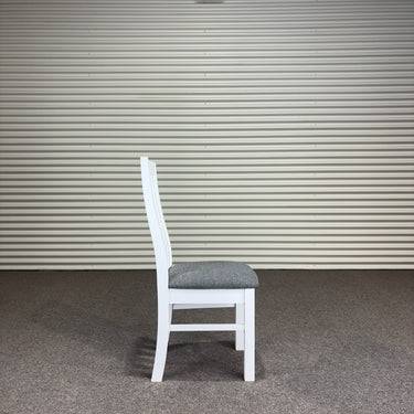 White wooden chair with a gray cushion against a corrugated metal wall. Kinloch Collection