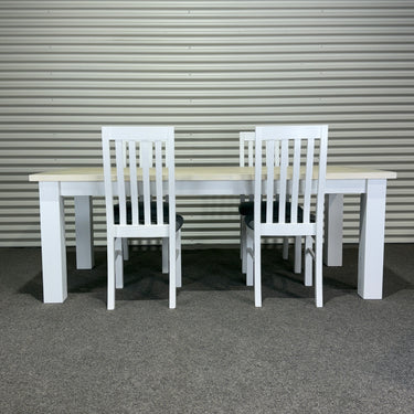 White dining table with four chairs against a corrugated metal wall. Kinloch collection
