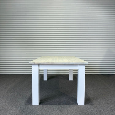 White table with a light wooden top against a corrugated metal wall.