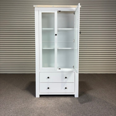 White cabinet with glass doors and drawers against a striped wall.