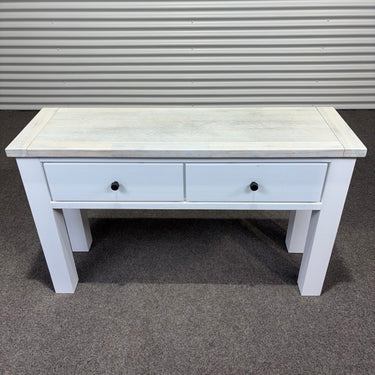 White wooden table with two drawers on a gray floor.