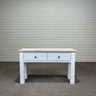 White wooden console table with two drawers against a corrugated metal wall.