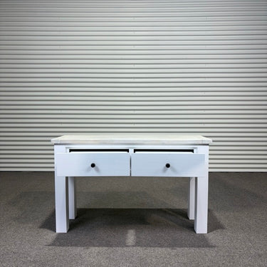 White wooden console table with two drawers against a corrugated metal wall.