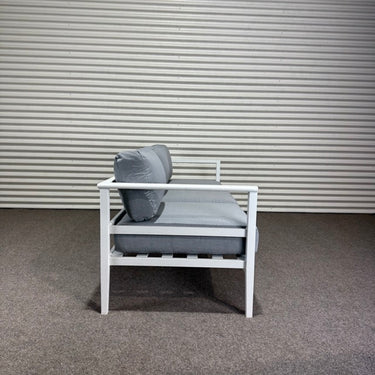 White chair with gray cushions against a corrugated metal wall.