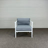 Chair with gray cushions on a concrete floor against a corrugated metal wall.