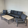 Outdoor furniture set with a sofa, chairs, and coffee table against a corrugated metal wall.