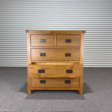 Wooden dresser with multiple drawers against a corrugated metal wall.