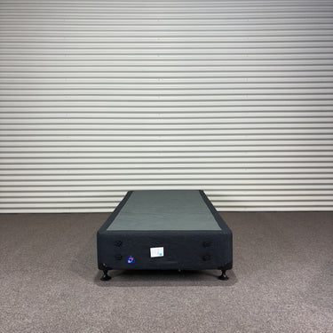 Charcoal fabric, bed base, made in New Zealand, pine wood, corner guard protection, on a gray floor with a striped wall background