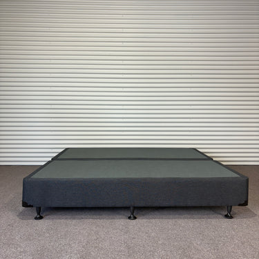 Charcoal fabric, bed base, made in New Zealand, pine wood, corner guard protection, on a gray floor with a striped wall background