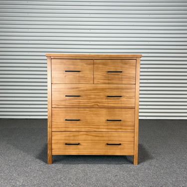 Wooden dresser with multiple drawers against a corrugated metal wall.