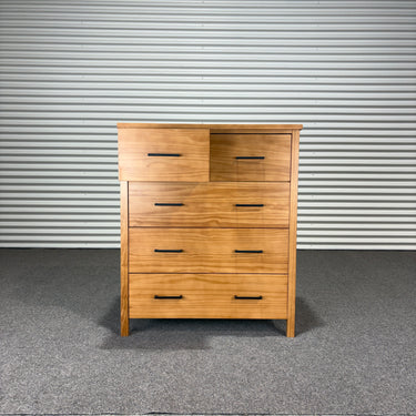 Wooden dresser with multiple drawers against a corrugated metal wall.