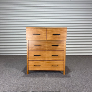 Wooden dresser with multiple drawers against a corrugated metal wall.