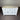 White wooden sideboard with three drawers and two doors against a corrugated metal wall.