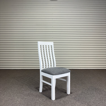 White chair with a gray cushion against a corrugated metal wall.