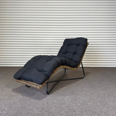 Chaise lounge with dark cushions on a gray floor against a metallic wall.