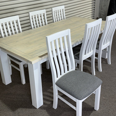 White chairs with gray cushions arranged around a wooden table on a concrete floor.