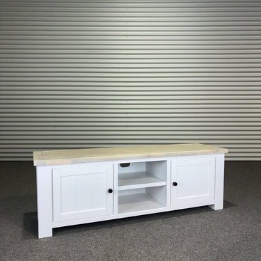 White wooden TV stand with a light wood top against a corrugated metal wall.