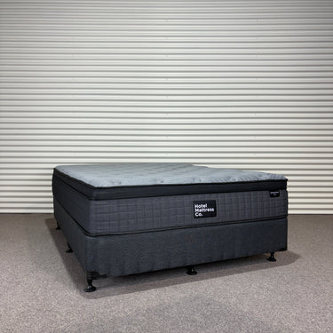 Workhorse LUX mattress front angle view showing quilted top, black fabric base, and brand label against corrugated backdrop