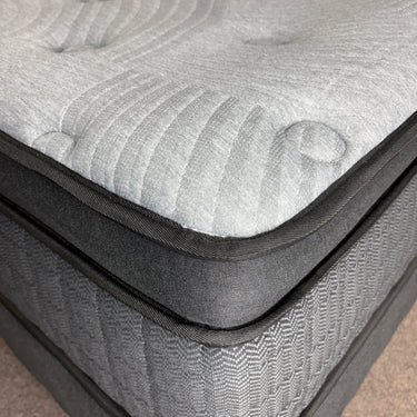 Close-up of Workhorse LUX mattress corner showing pillow top with grey quilted fabric, black piping, and textured stitching details